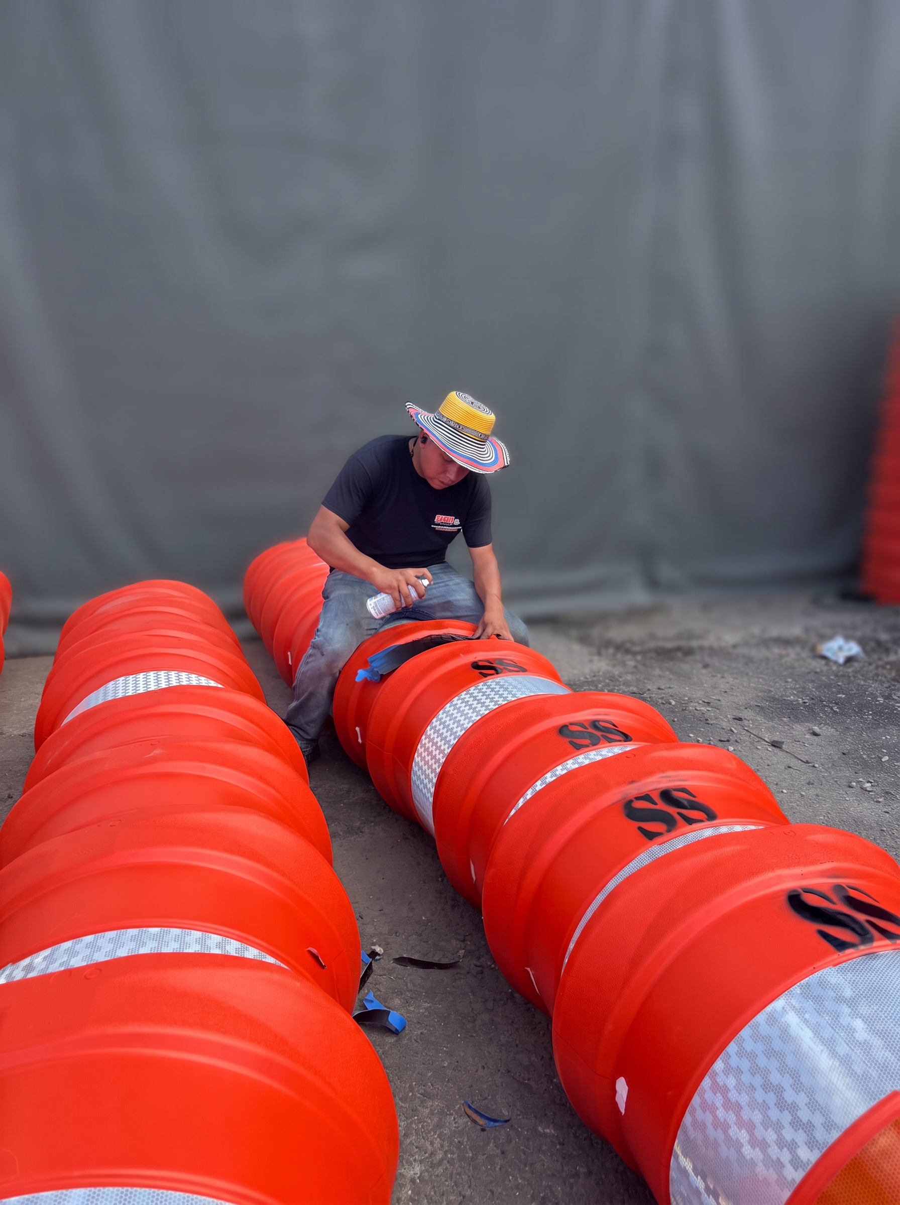Highway Traffic Control crew member painting a channelizer drum with the garage background softly blurred